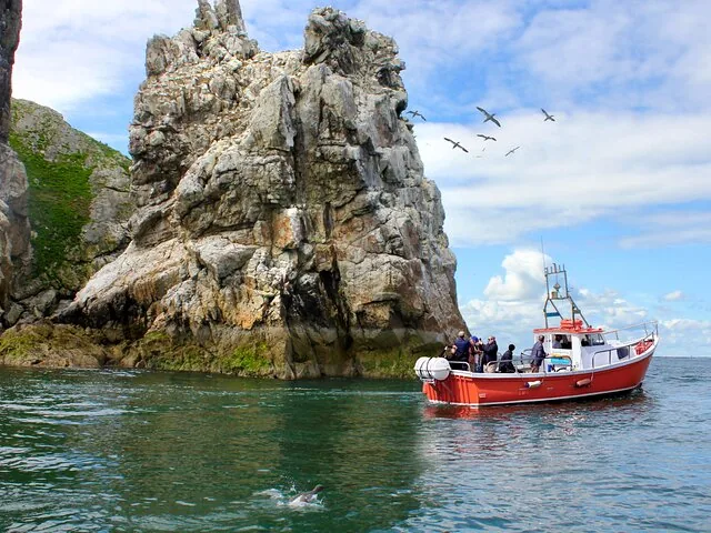 Red and white tour boat near a large rocky sea stack