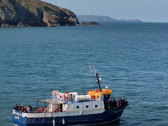 Small passenger boat sailing in the sea near a rocky coastline