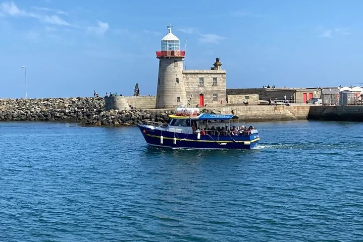 Small blue boat carrying passengers near a stone lighthouse and pier
