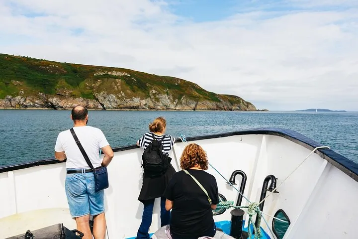 Three people standing on the bow of a boat looking at an island