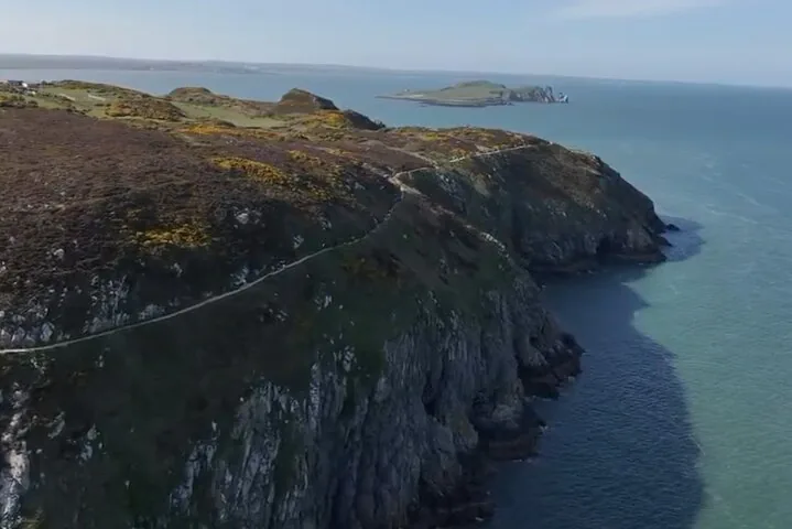 Aerial view of a coastal path along a cliff leading towards an island
